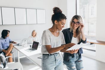 Two women looking at paper together in office smiling-1