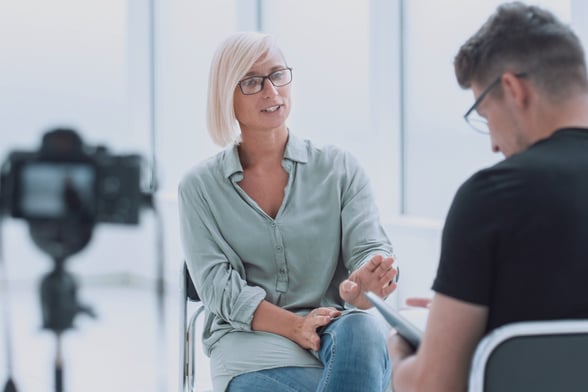 Woman talking to man in chair with camera recording-1