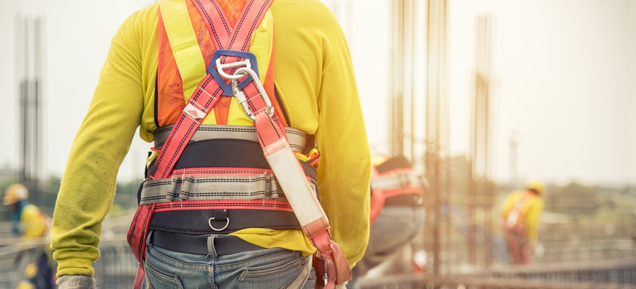 A construction worker wearing a protective safety harness walks to the job site.